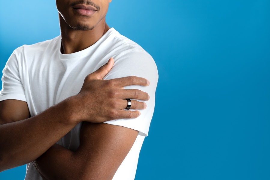 A close-up, high-contrast studio shot of a model wearing a sleek smart ring, utilizing a bold blue background to emphasize the product design.